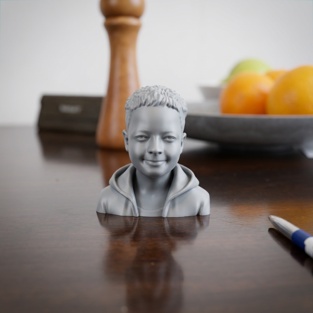 3D-printad porträttbyst av ett barn i huvtröja, i grå matt finish, på ett bord